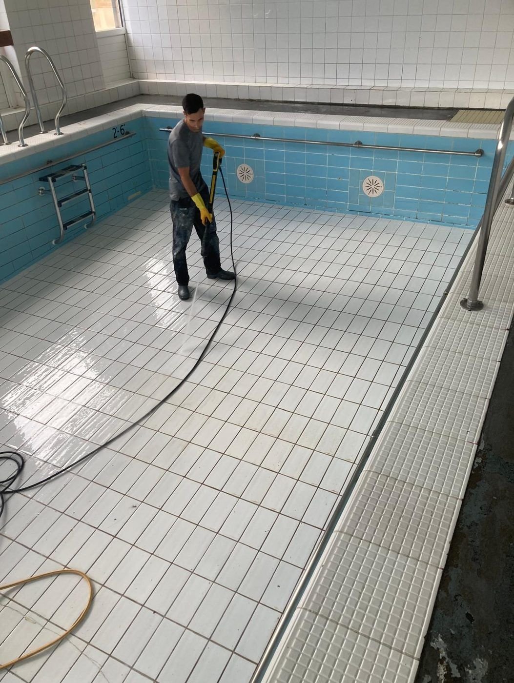 Tiled pool floor being pressure washed during a deep clean