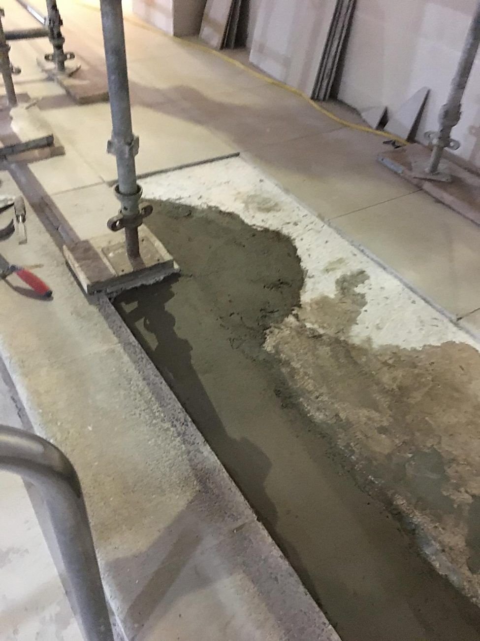 Fresh screed laid along a channel beside a pool, ready for tiling